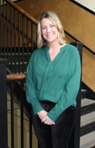 a blonde woman wearing a green shirt stands in a sunlit stairway