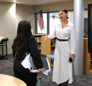 a woman wearing a white dress talks to a young female student