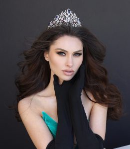 a woman with dark hair wars black gloves, a green dress and a tiara crown