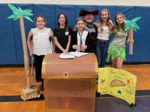 six elementary students pose with treasure island props around them
