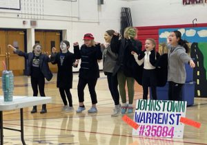 seven young students perform a skit in costume, inside a gymnasium