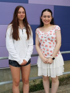 two teenaged girls pose outside in front of a purple wall
