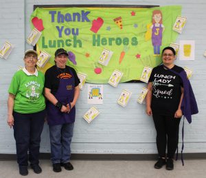 three women stand in front of a bulletin board that says "Thank you lunch heroes"