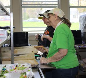 two women serve food in a cafeteria line