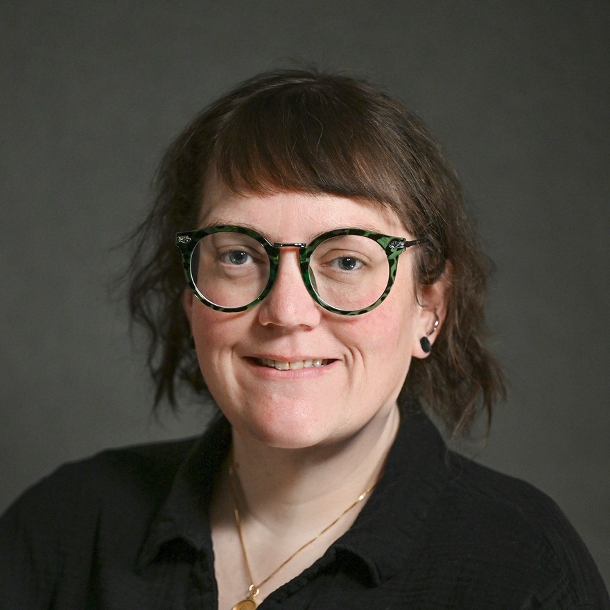 a woman with short dark hair and green glasses smiles at the camera