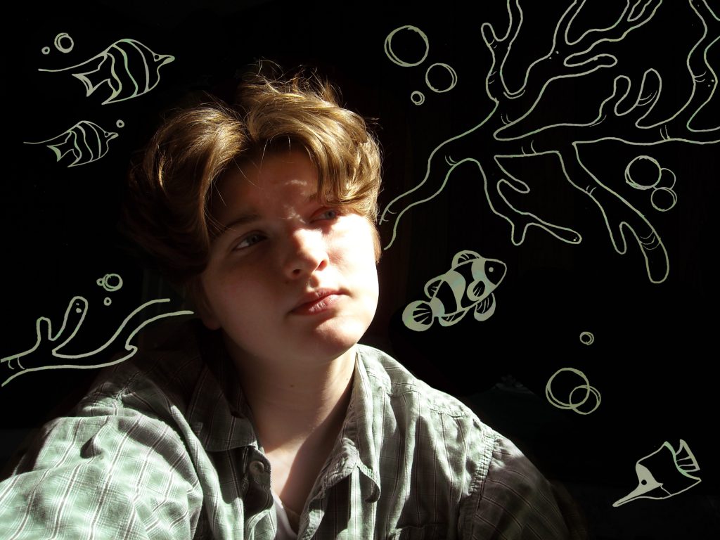 a young man with shaggy brown hair poses in front of a black background with green aquatic drawings