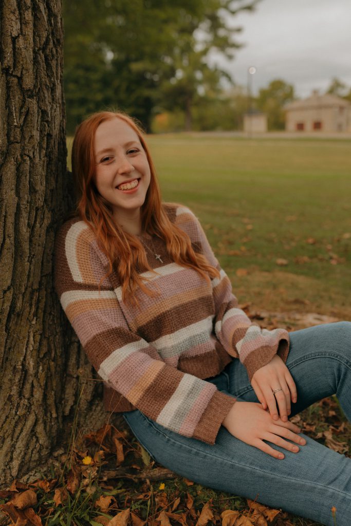 a young girl with red hair leans against a tree