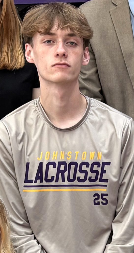 a young man wears a grey shirt that reads "Lacrosse"