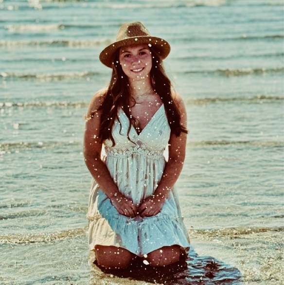 a girl wearing a sundress and hat poses on a beach