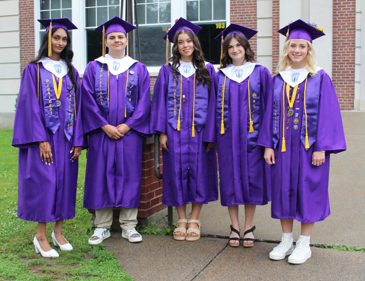 a group of five graduating seniors wear purple graduation gowns outside of a school