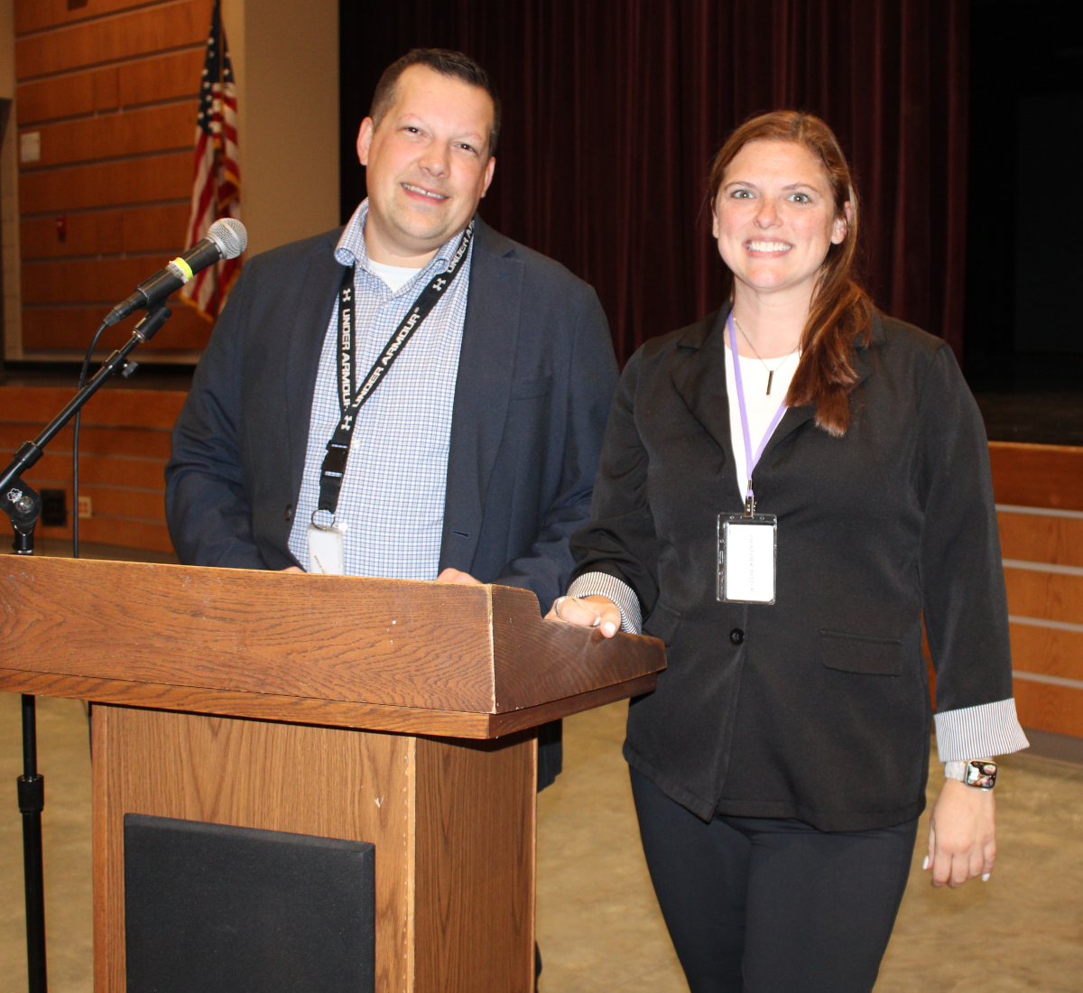 an adult man and woman stand next to each other in an auditorium standing at a podium