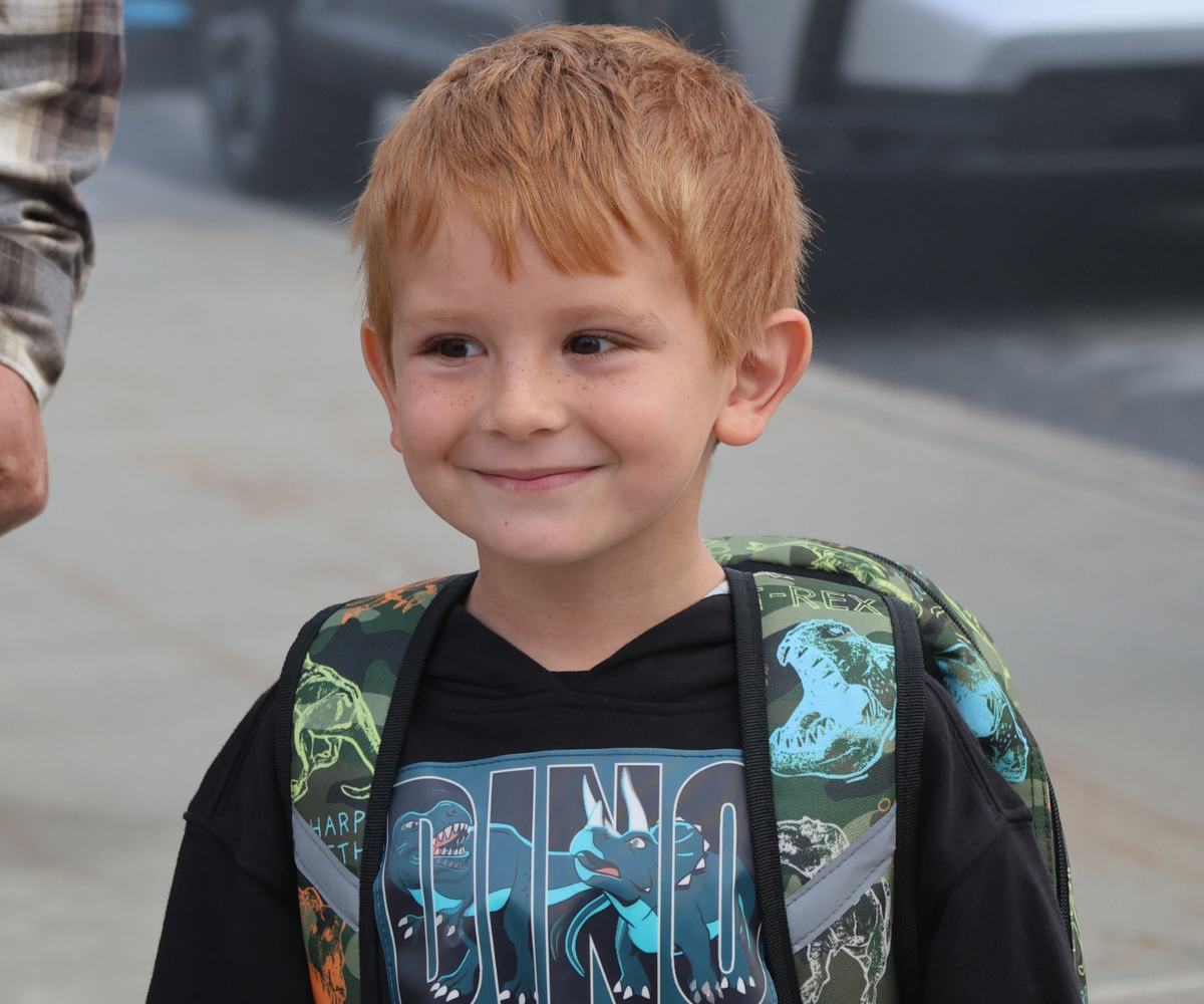 a young boy with a backpack smiles outside
