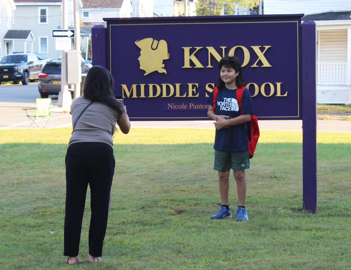 a woman takes her child's picture in front of the school