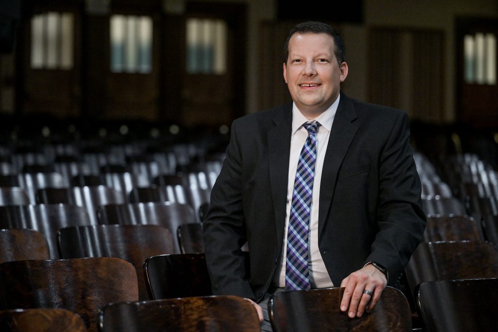 an adult man with a suit and tie sits in an empty auditorium