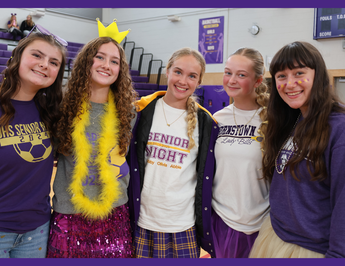a group of teenage girls dressed in purple and yellow pose in a gymnasium