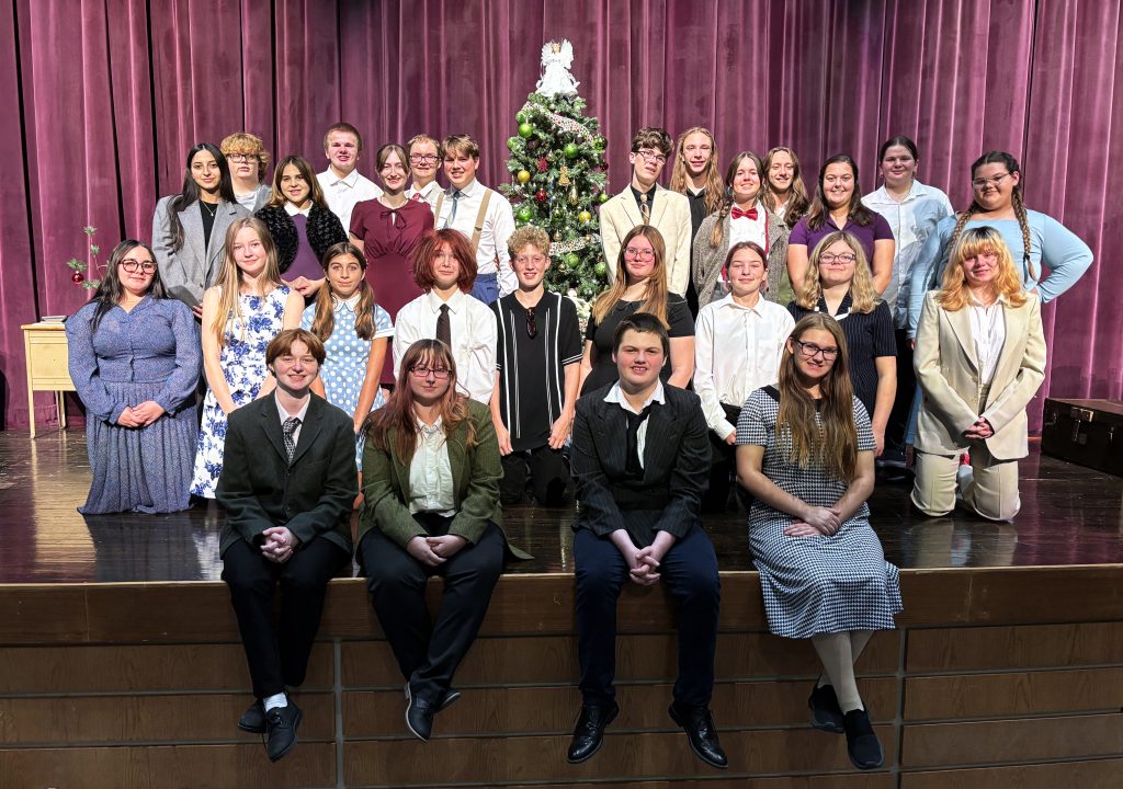 a group of young actors pose on a theatrical stage in front of a Christmas tree