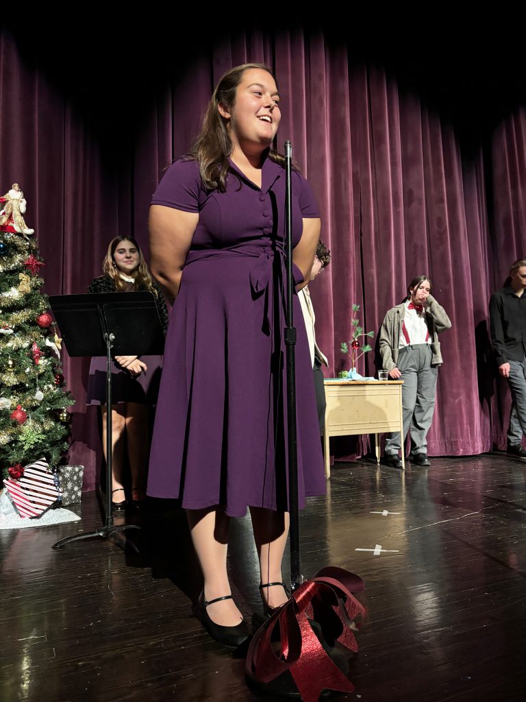 a young girl with a purple dress speaks into a microphone on a stage