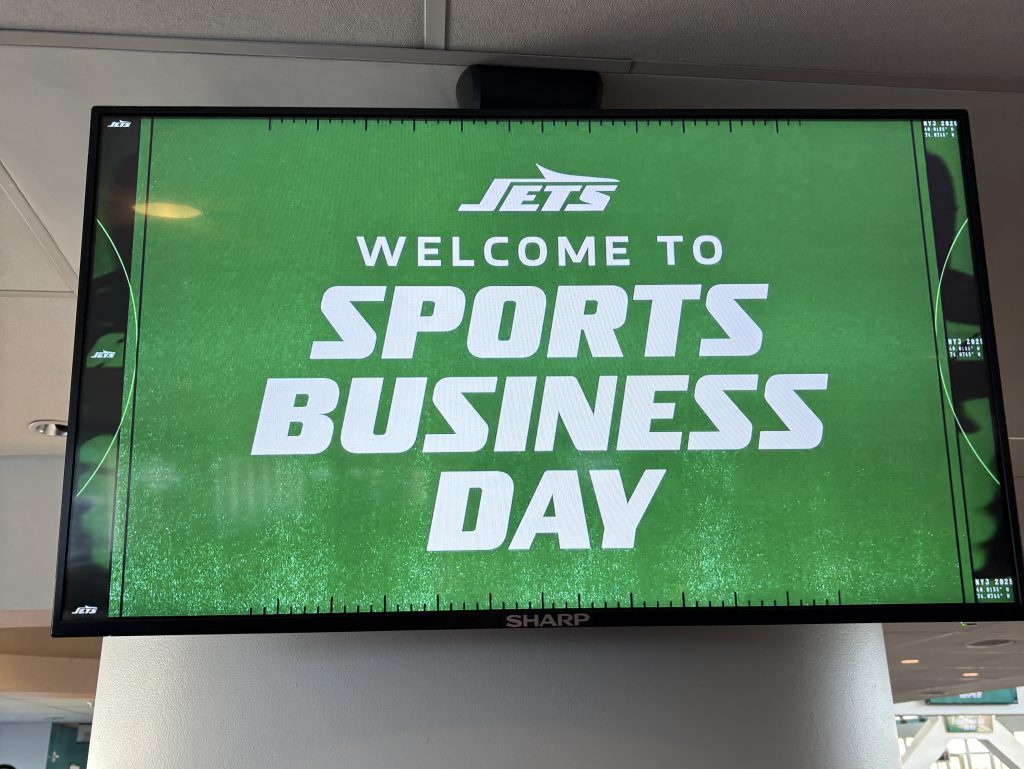 a digital sign reads "Jets Welcome to Sports Business Day" 