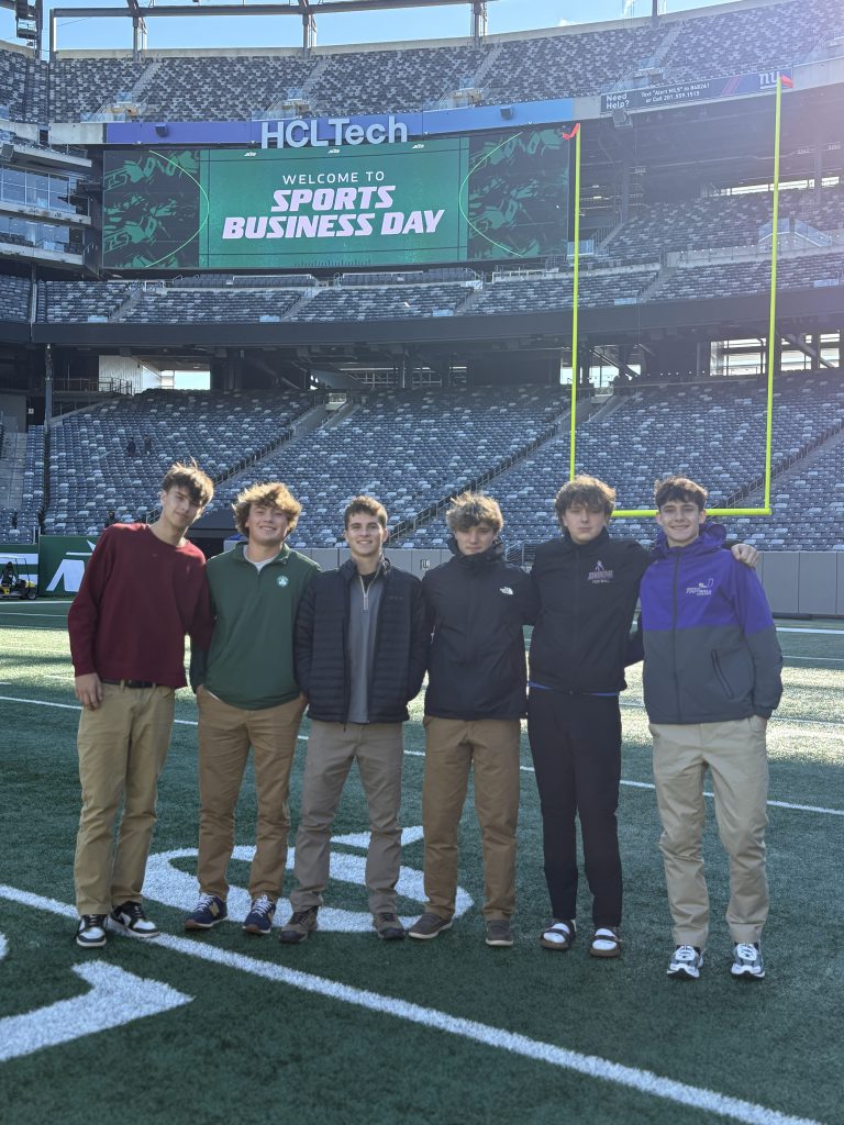 male teen students stand on a turf football field in an empty stadium