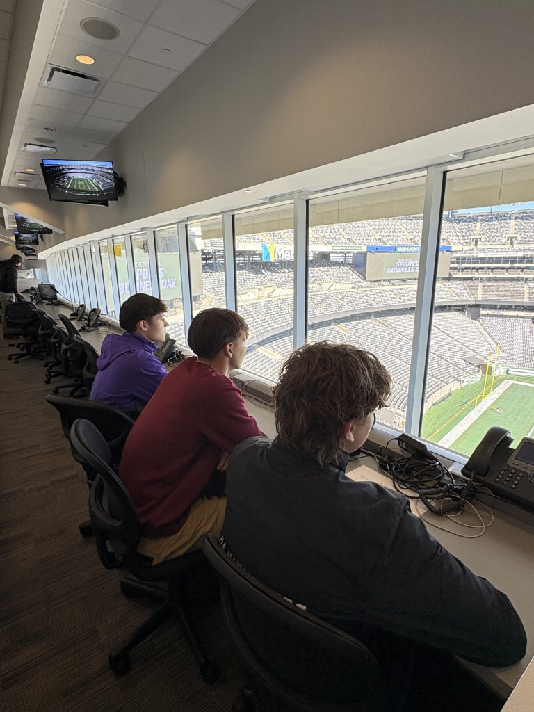 teenaged boys sit inside a press box at a professional football stadium