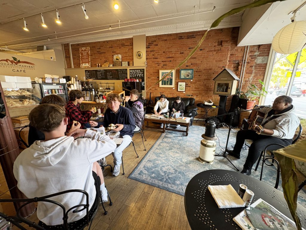 students sit in a cafe eating lunch while a person plays guitar