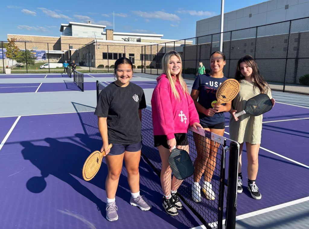 four young teen females pose on an outside purple pickle ball court