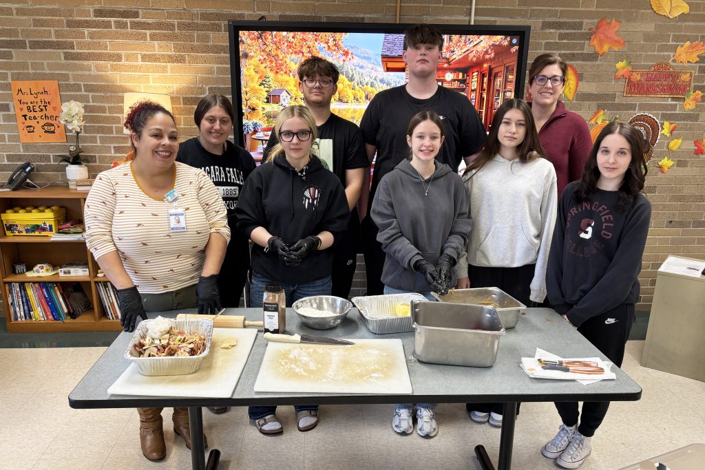a group of students pose in a classroom behind a table with food ingredients on it
