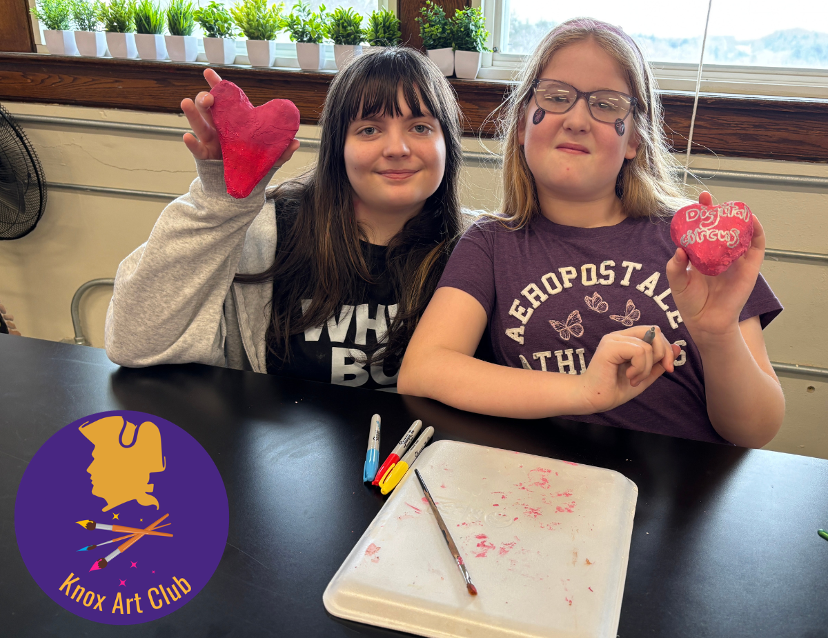 two young girls hold up pink paper mache hearts with a purple and gold logo that reads "Knox Art Club"