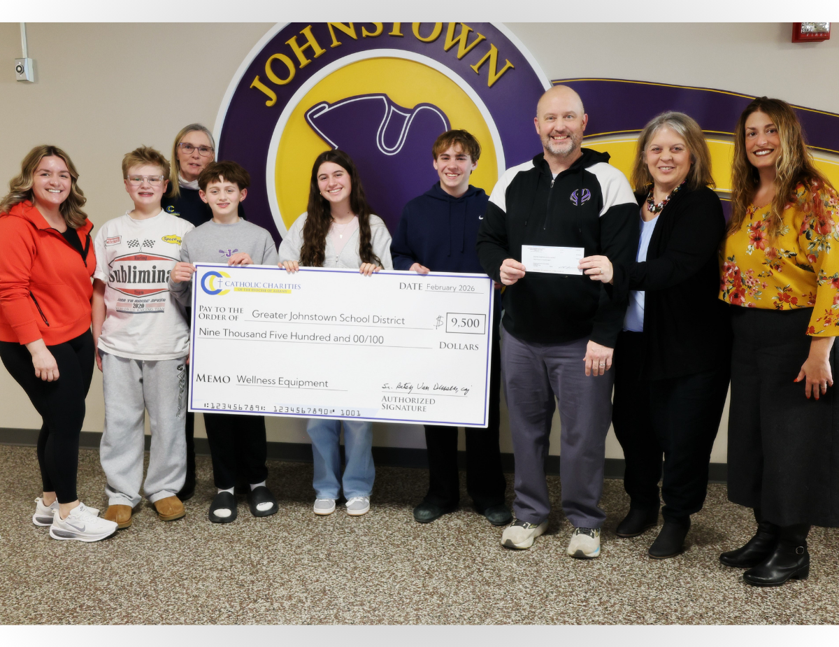 teens and adults pose in front of a school logo holding an oversized check
