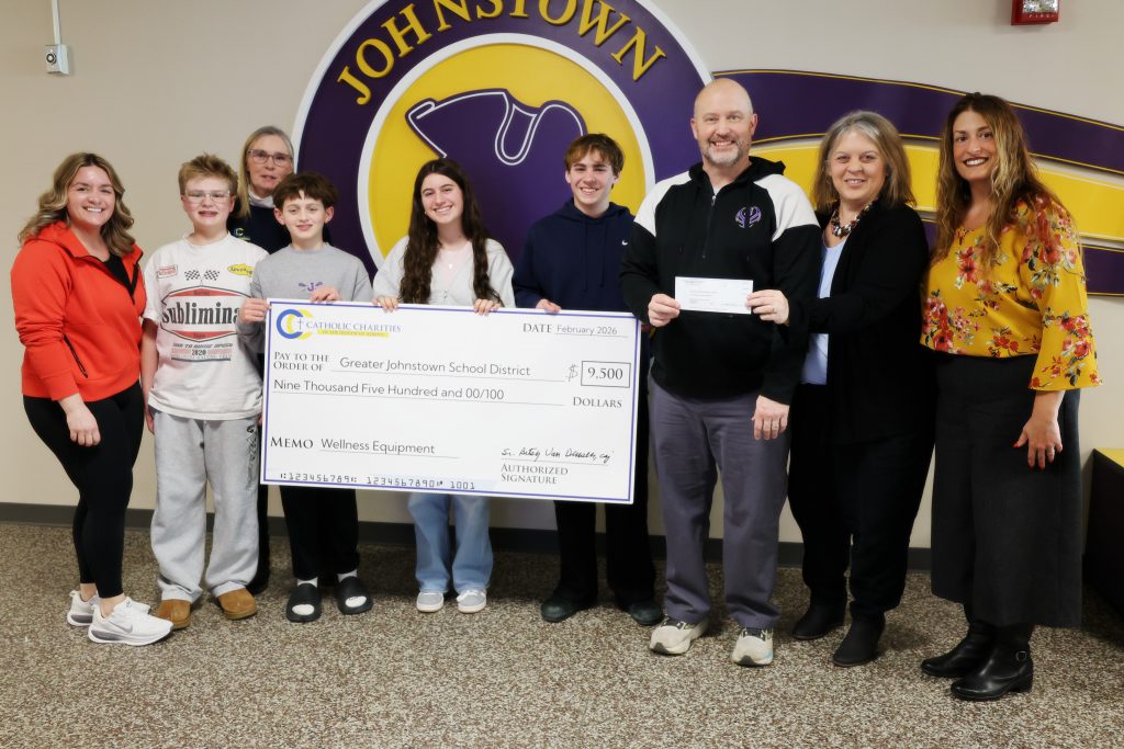 a group of adult and students hold an oversized check in the hallway of a school