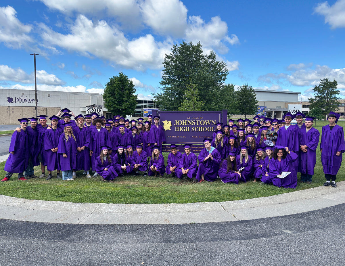 a group of graduates wearing purple gowns and caps pose outside near their high school sign