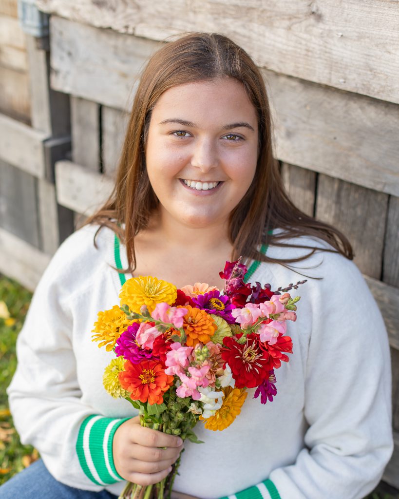 a young girl poses outside on a bench holding a bouquet of flowers