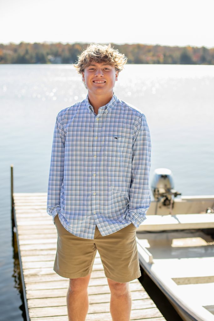 a young man with a checkered shirt poses on a dock near a lake