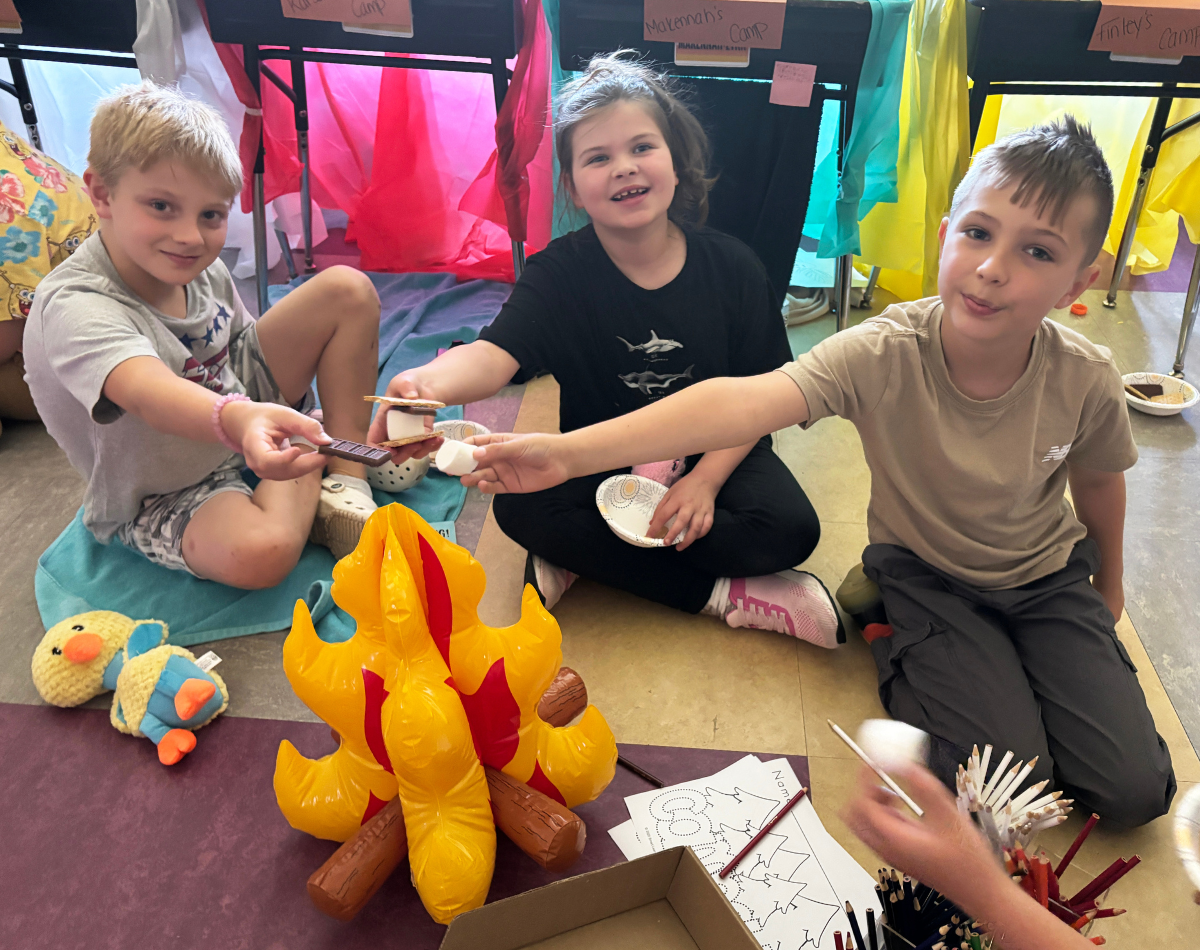 young students pretend to roast marshmallows over a fake fire in a classroom 