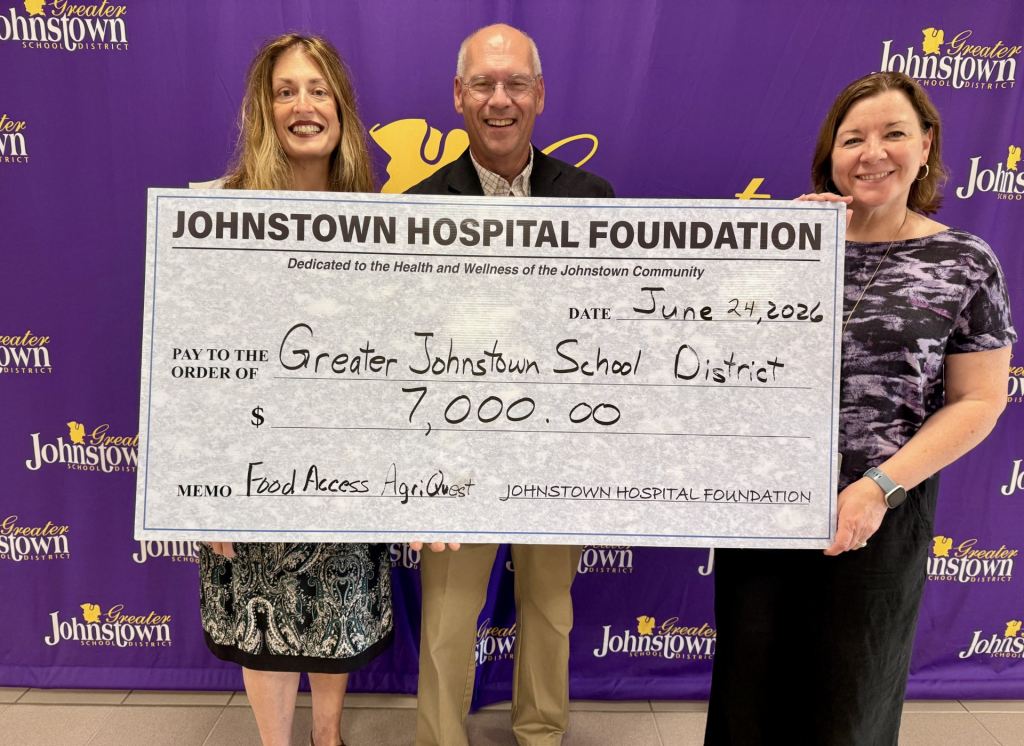 two women and a man stand behind an oversized check